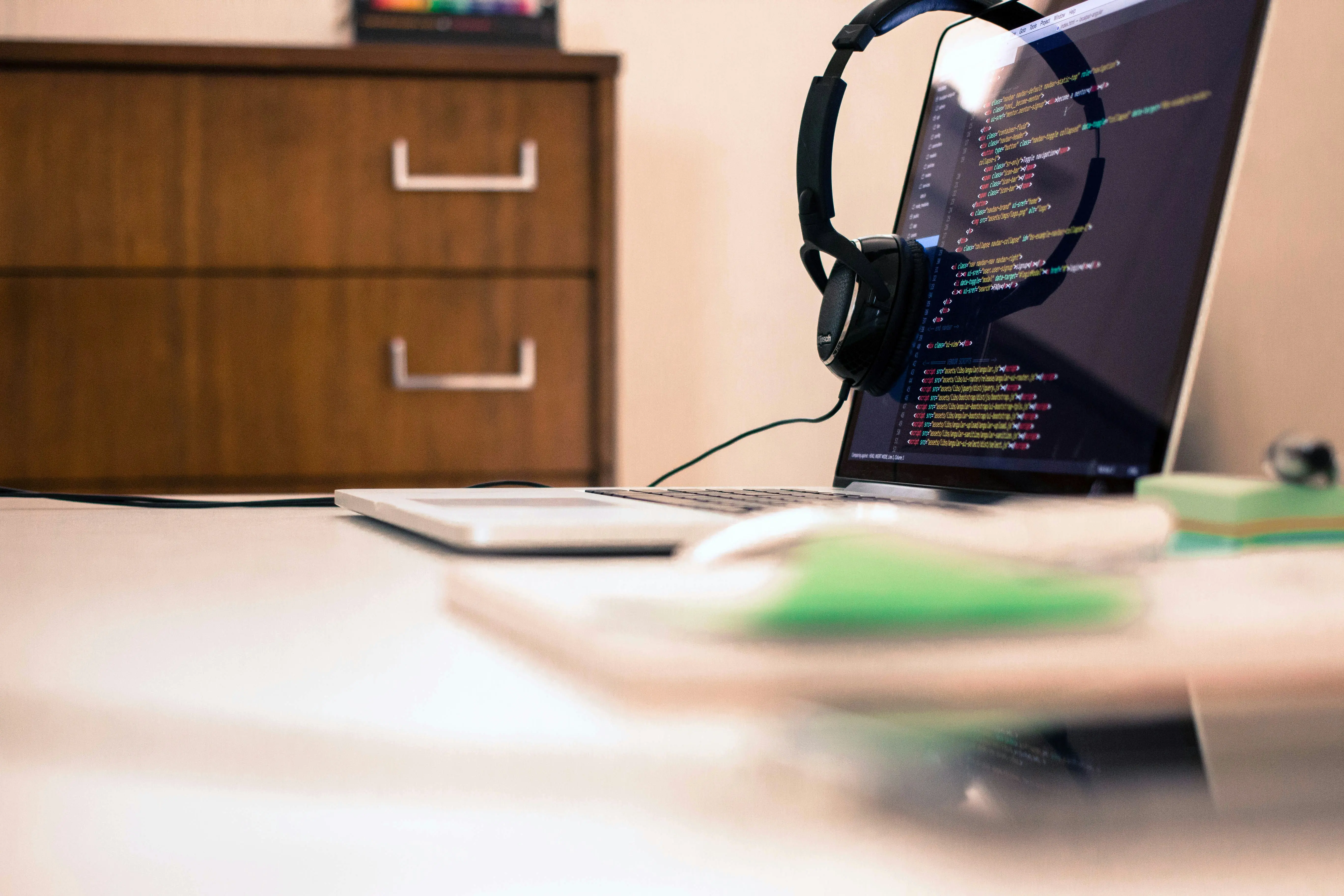 Laptop with headphones showing frontend markup in an editor