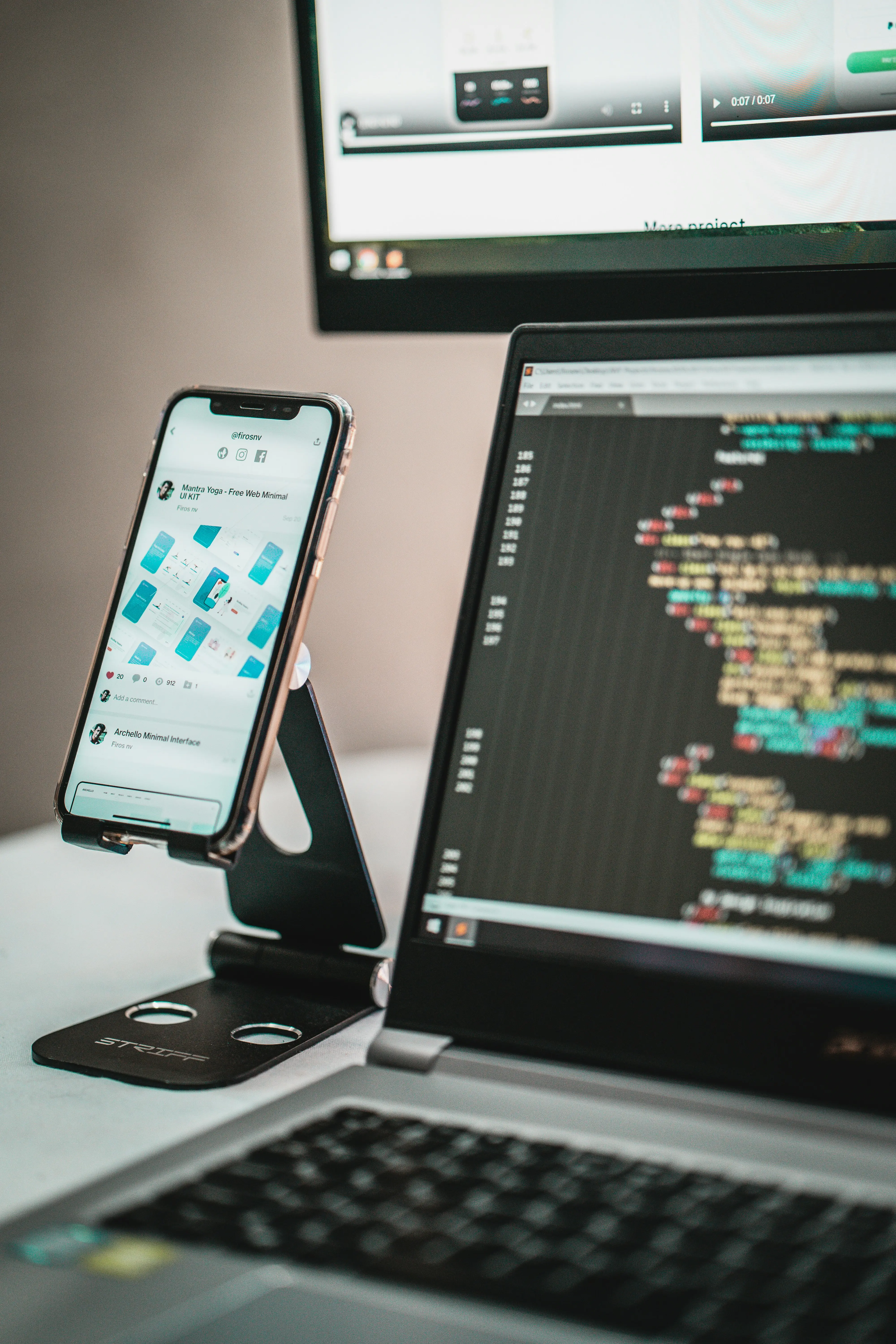 Phone and laptop on a desk showing app UI designs and code